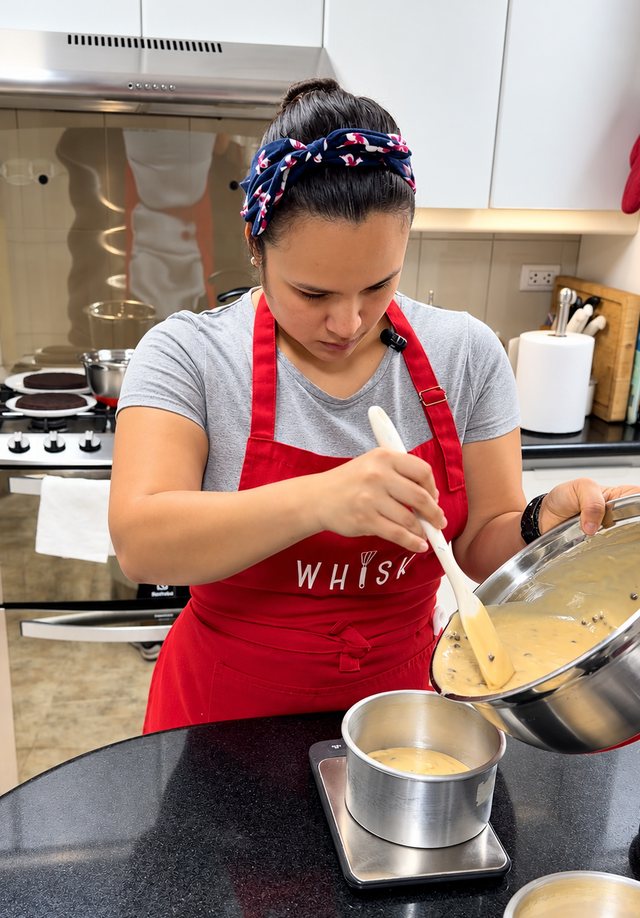 Alicia Chong con mandil rojo de Whisk vertiendo la masa de una torta en los moldes